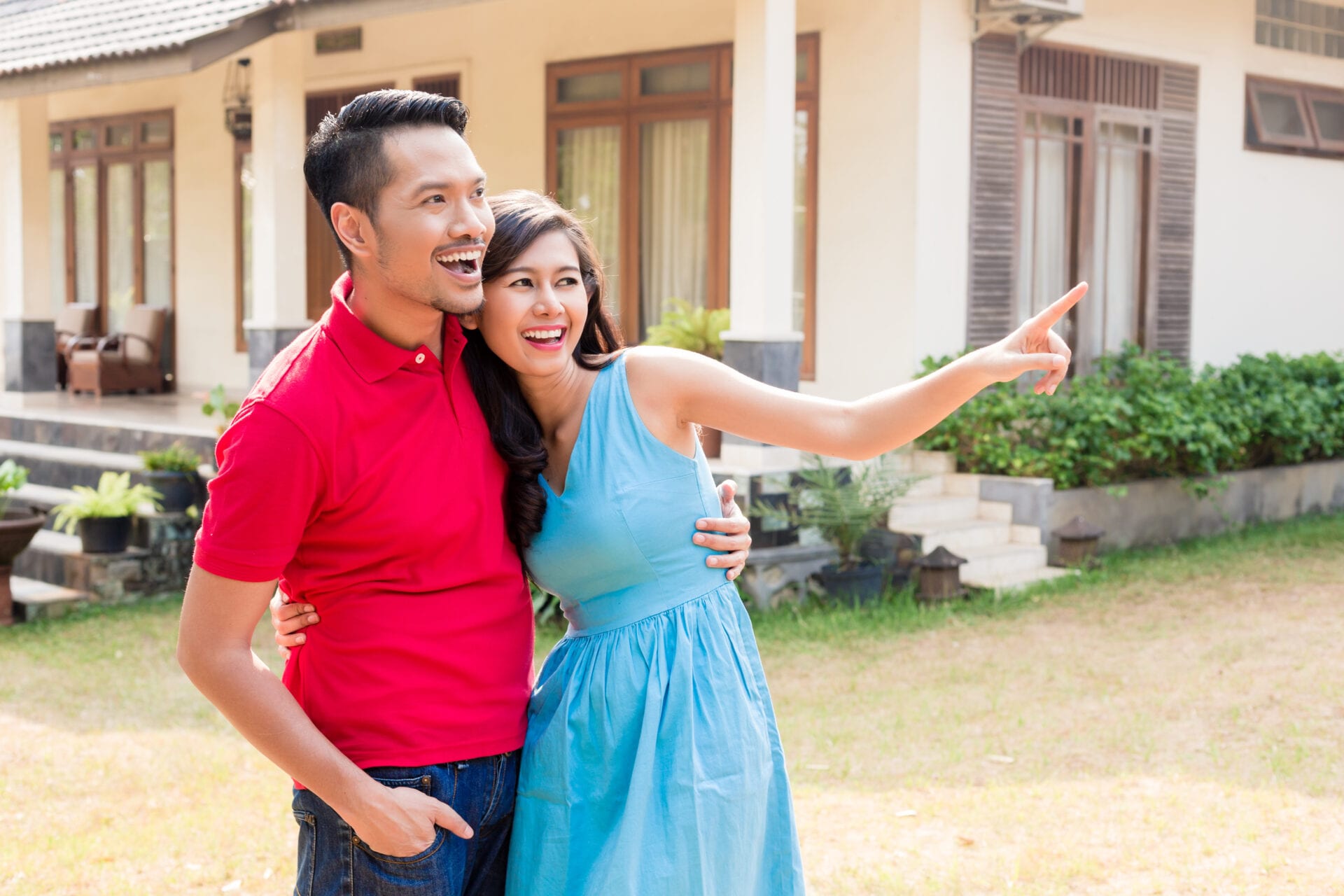 Cheerful young couple looking in the same direction in front of a cozy residential property